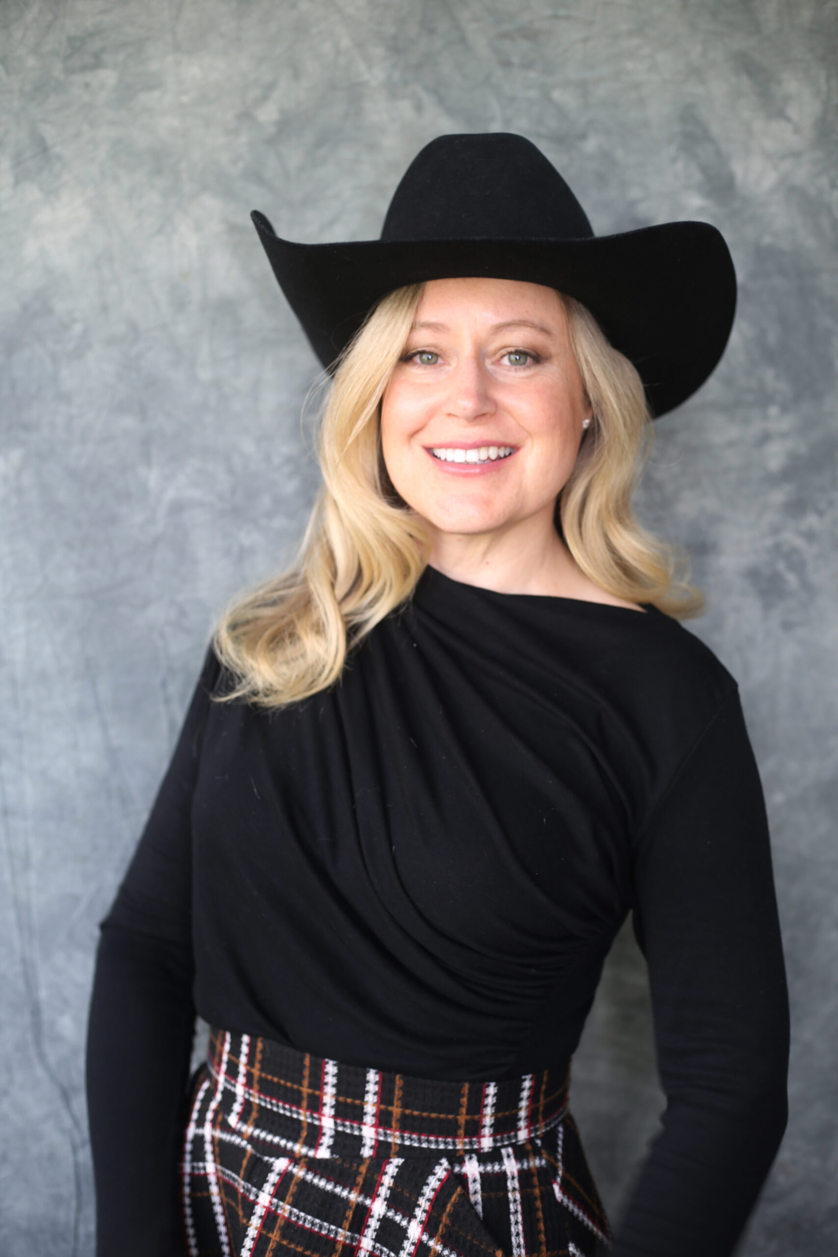 Headshot of Amy Fast, wearing all black attire and a black cowboy hat.