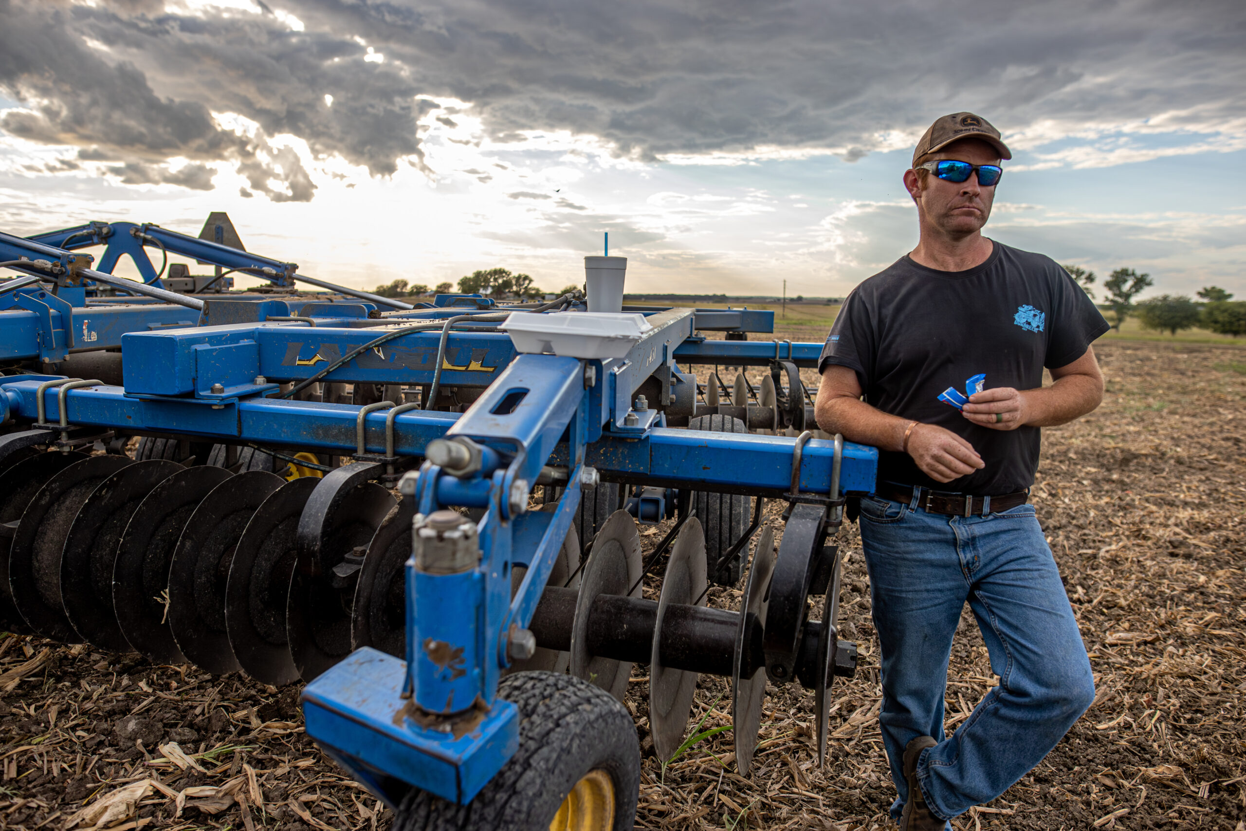 farmer in a ballcap, jeans and tshirt eating a meal in the field